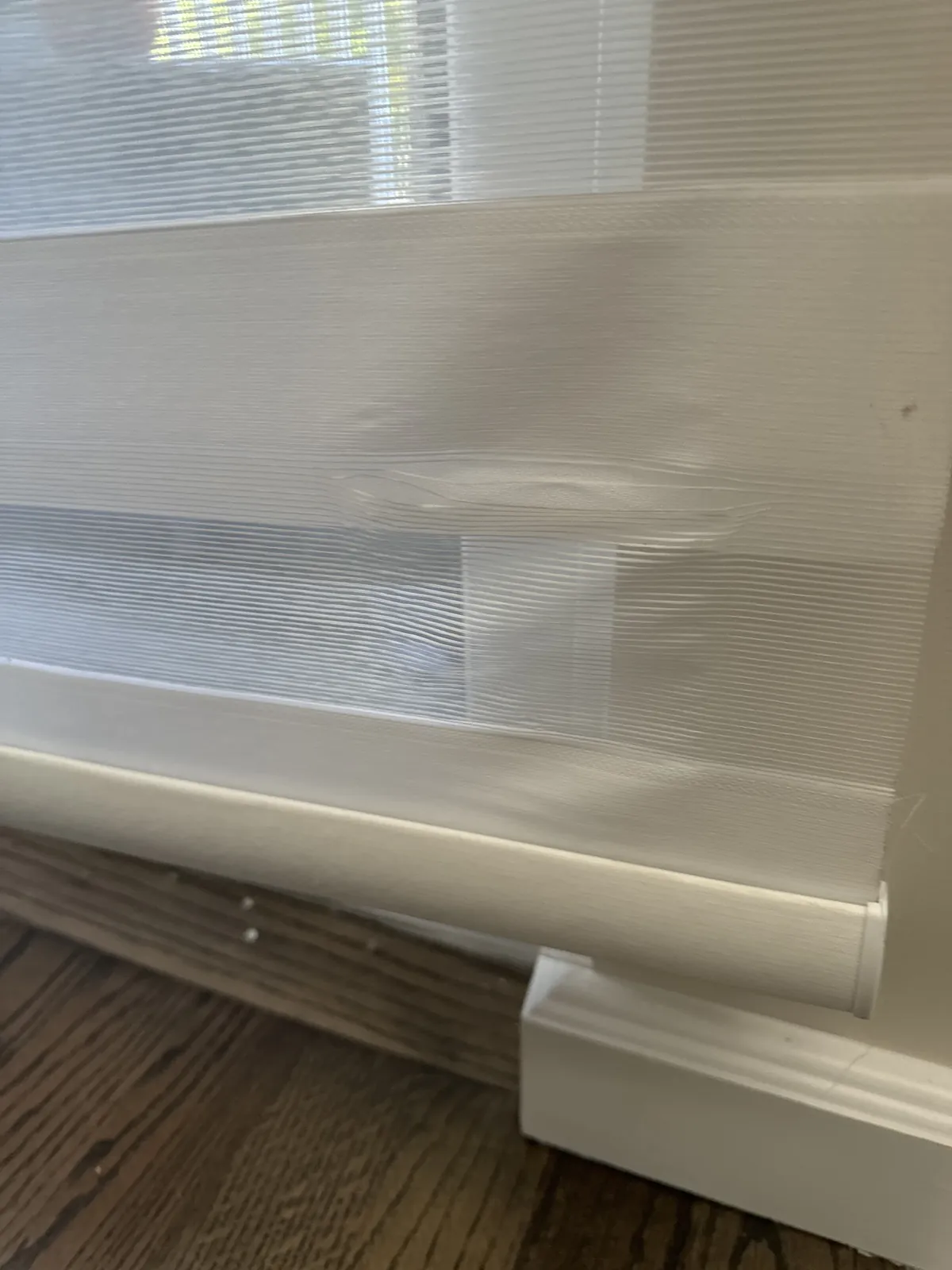 A fabric roller shade partly lowered in a bay window, hanging unevenly