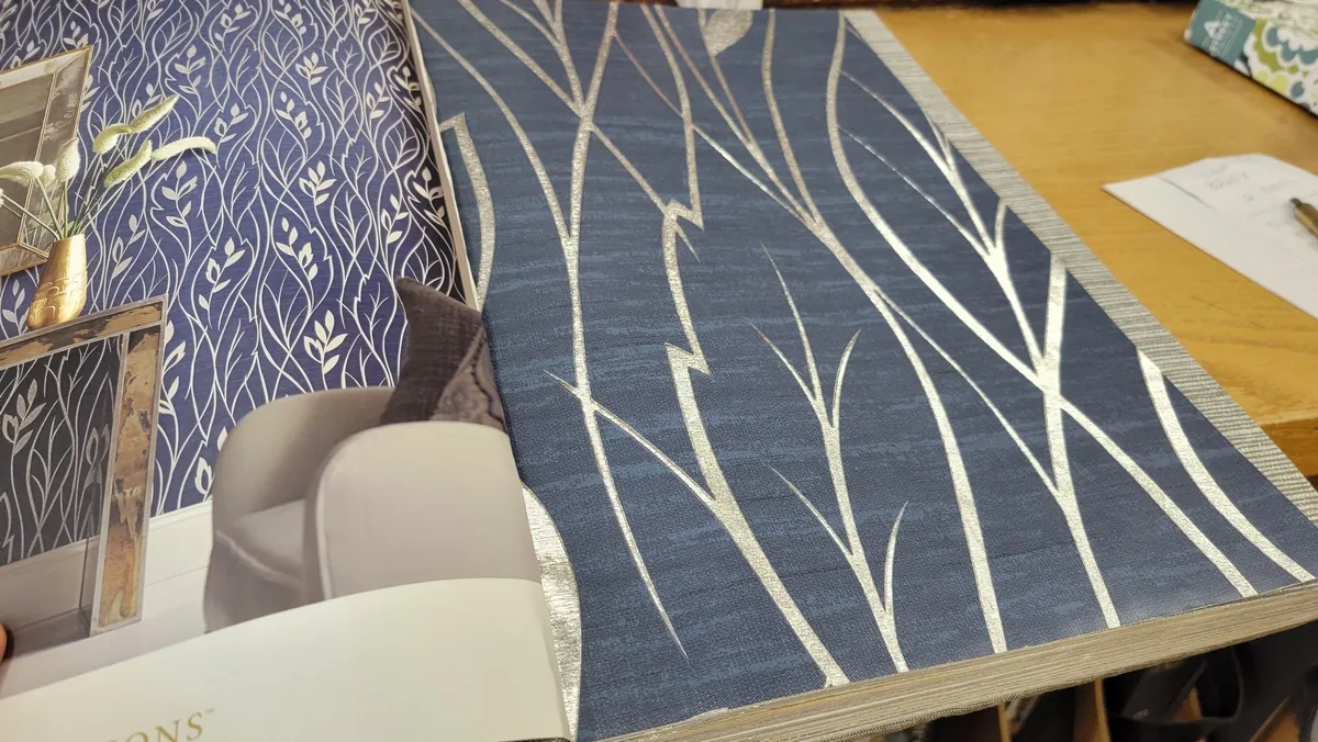 Rolls and sample books of patterned wallpaper on a showroom shelf